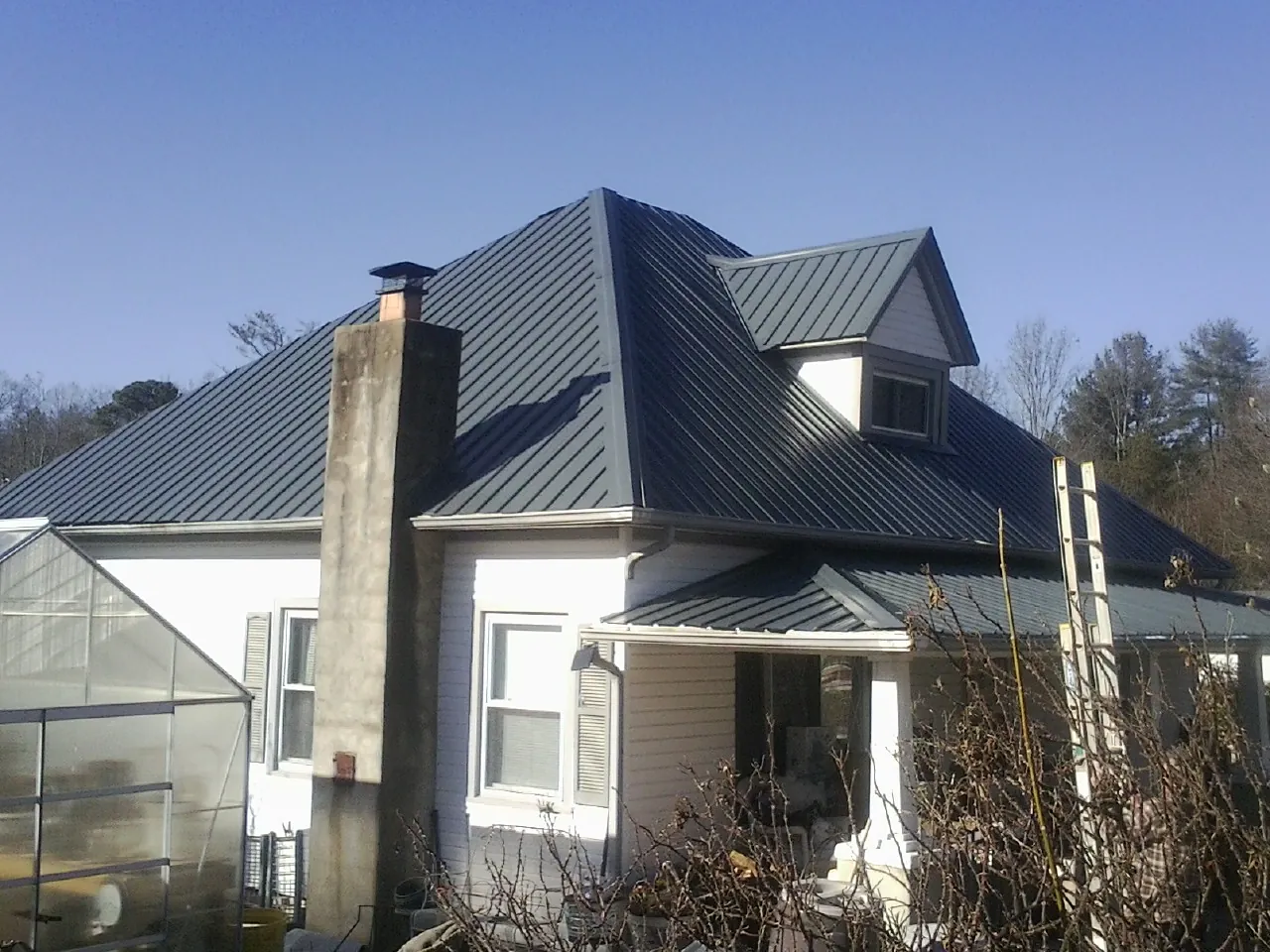 Dark blue standing seam metal roof on a white farmhouse with dormer — Slate & Tile Roof Repair by Roofing Brothers in Rowan
