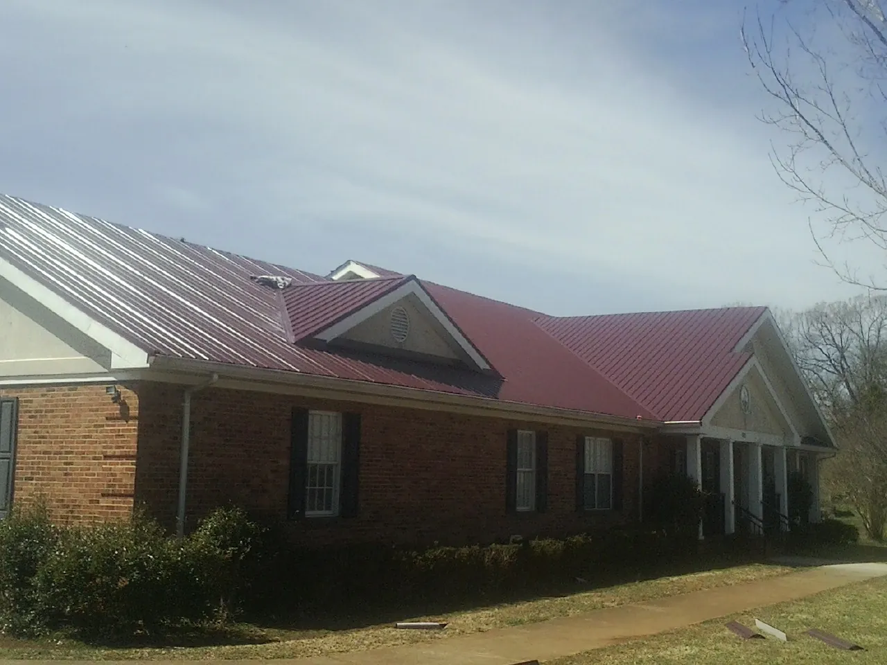 Red metal roof with gabled entries on a long brick building, from a Hail Damage Roof Repair job in Rowan