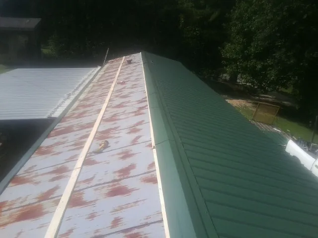 Old rusted panels beside newly installed green metal roofing — Wind Damage Roof Repair by Roofing Brothers in Rowan