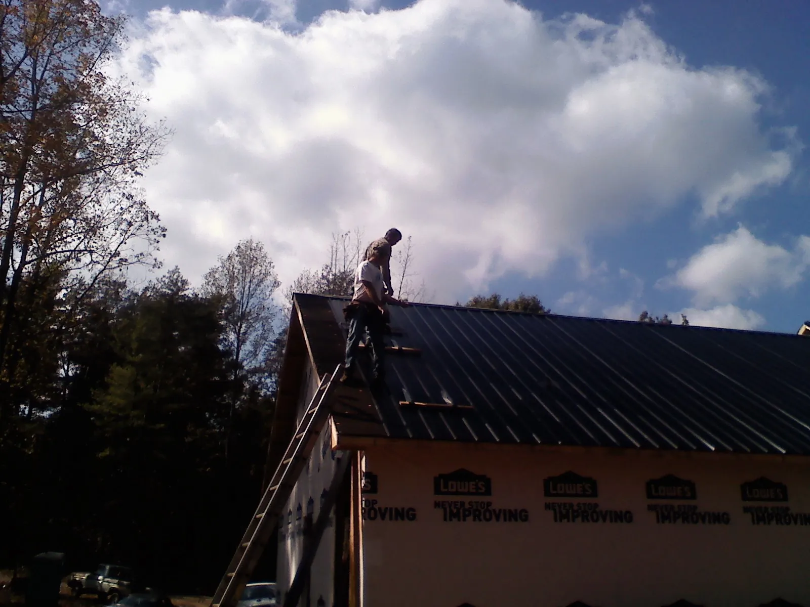 Roofer fastening dark metal panels high against a cloudy sky, from a Roof Inspection job in Rowan