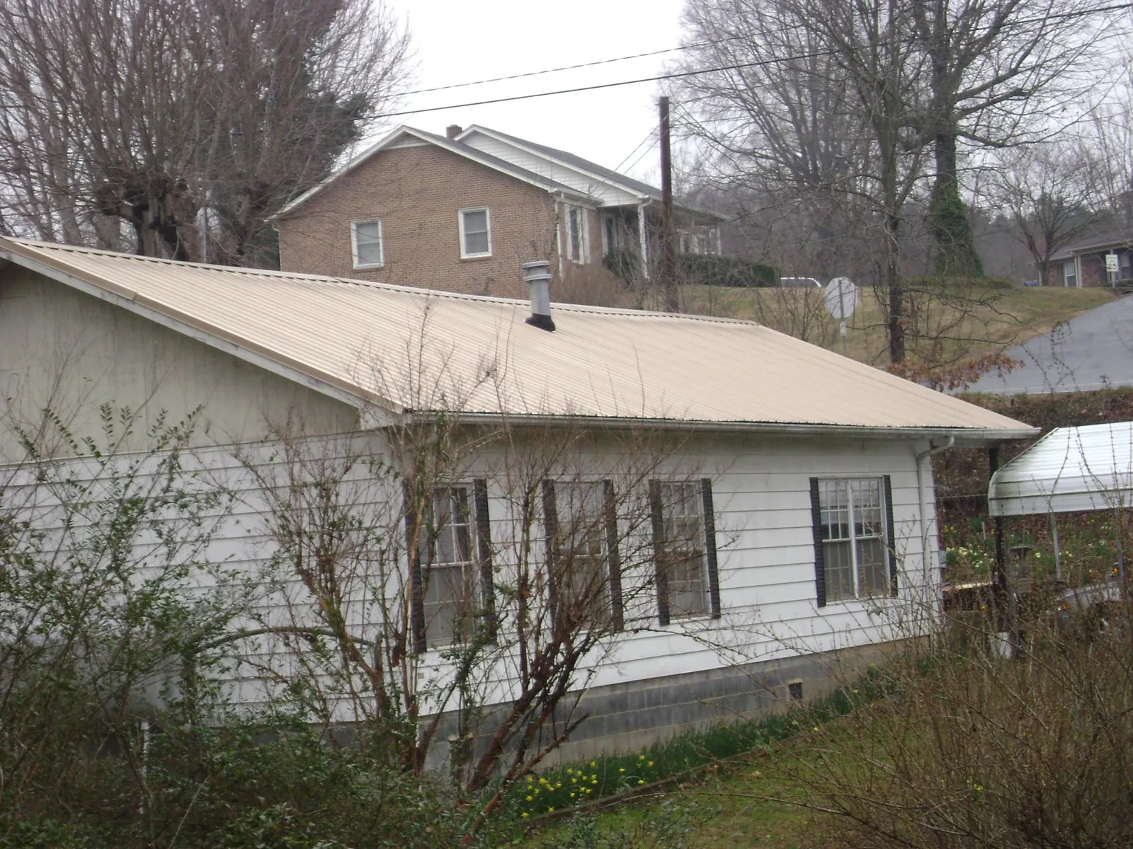 Tan metal roof on a white sided house set into a hillside — Commercial Roofing by Roofing Brothers in Rowan